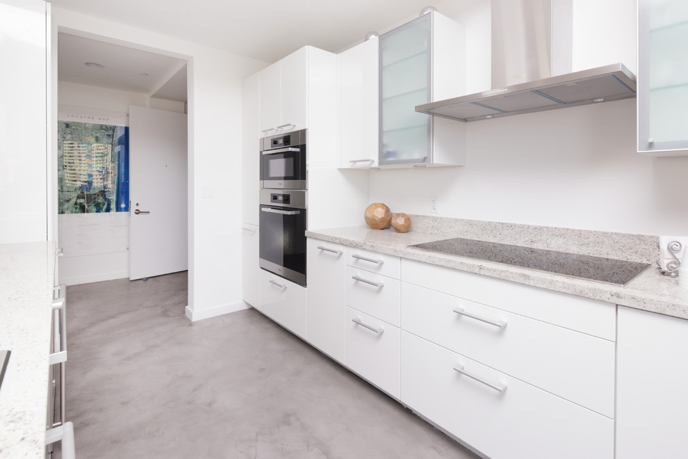 This is an example of a medium sized contemporary kitchen in Miami with flat-panel cabinets, white cabinets, granite worktops, stainless steel appliances and concrete flooring.