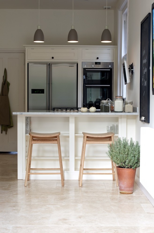 Foto di una cucina design chiusa e di medie dimensioni con ante in stile shaker, ante bianche, top in marmo, elettrodomestici in acciaio inossidabile, pavimento in travertino e penisola