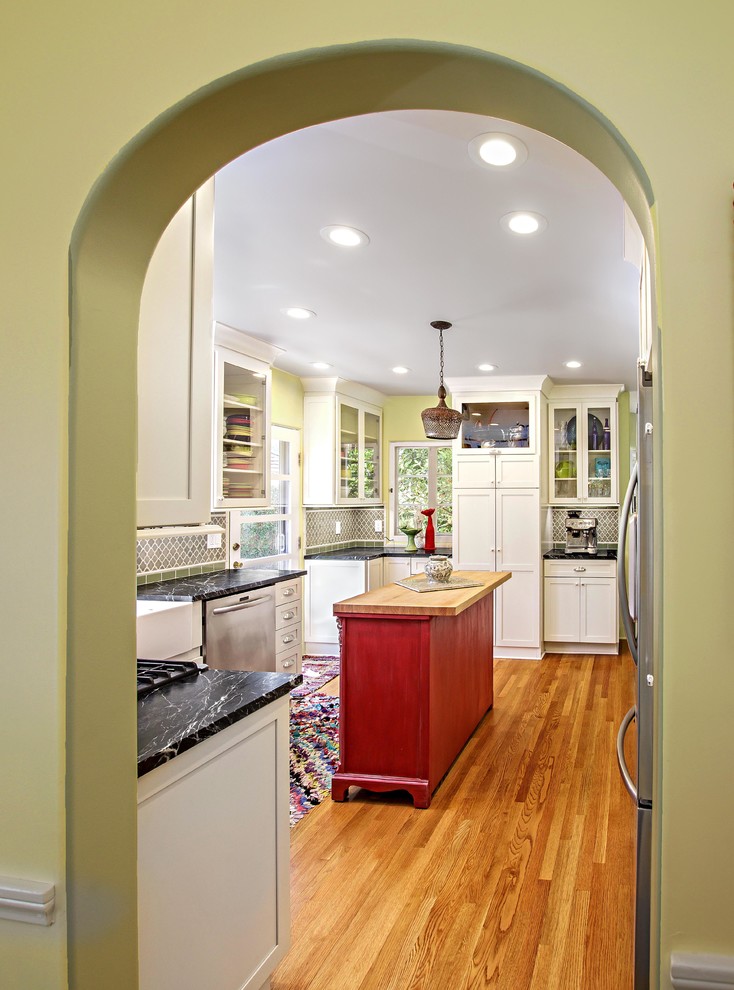 Kitchen - mid-sized eclectic l-shaped medium tone wood floor kitchen idea in Orange County with a farmhouse sink, shaker cabinets, white cabinets, soapstone countertops, green backsplash, glass tile backsplash, stainless steel appliances and an island