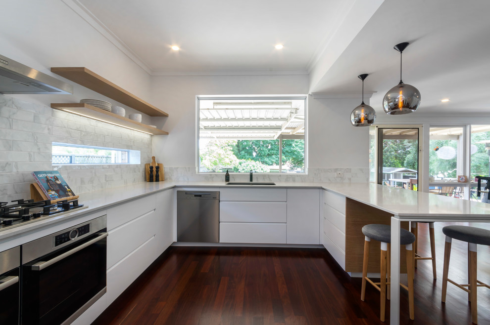 Inspiration for a large contemporary u-shaped kitchen pantry in Perth with a double-bowl sink, white cabinets, engineered stone countertops, white splashback, metro tiled splashback, stainless steel appliances, dark hardwood flooring, no island, brown floors and white worktops.