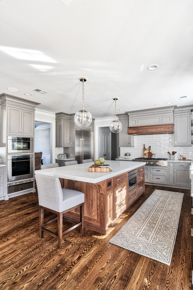 Inspiration for a mid-sized transitional u-shaped medium tone wood floor and brown floor kitchen pantry remodel in Other with a farmhouse sink, beaded inset cabinets, gray cabinets, solid surface countertops, gray backsplash, subway tile backsplash, stainless steel appliances, an island and white countertops