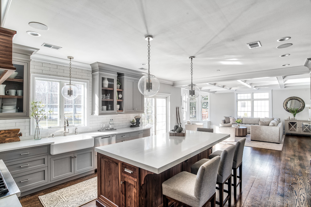 Photo of a medium sized classic u-shaped kitchen pantry in Other with a belfast sink, beaded cabinets, grey cabinets, composite countertops, grey splashback, metro tiled splashback, stainless steel appliances, medium hardwood flooring, an island, brown floors and white worktops.