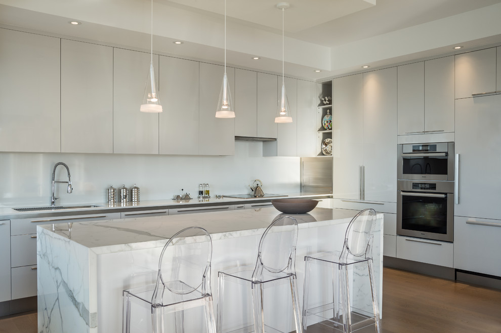 Inspiration for a medium sized contemporary l-shaped kitchen in Toronto with a submerged sink, flat-panel cabinets, white cabinets, marble worktops, white splashback, integrated appliances, medium hardwood flooring and an island.