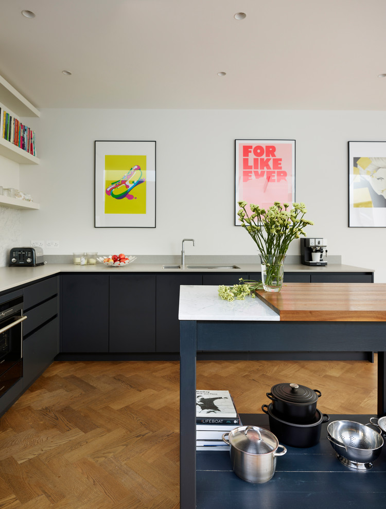 This is an example of a large scandinavian l-shaped open plan kitchen in London with flat-panel cabinets, blue cabinets, composite countertops, medium hardwood flooring, an island, beige floors and white worktops.
