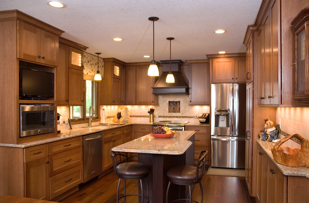 Cette photo montre une cuisine américaine craftsman en U et bois brun de taille moyenne avec un évier 2 bacs, un placard à porte plane, un plan de travail en granite, une crédence beige, une crédence en carrelage de pierre, un électroménager en acier inoxydable, parquet foncé et îlot.