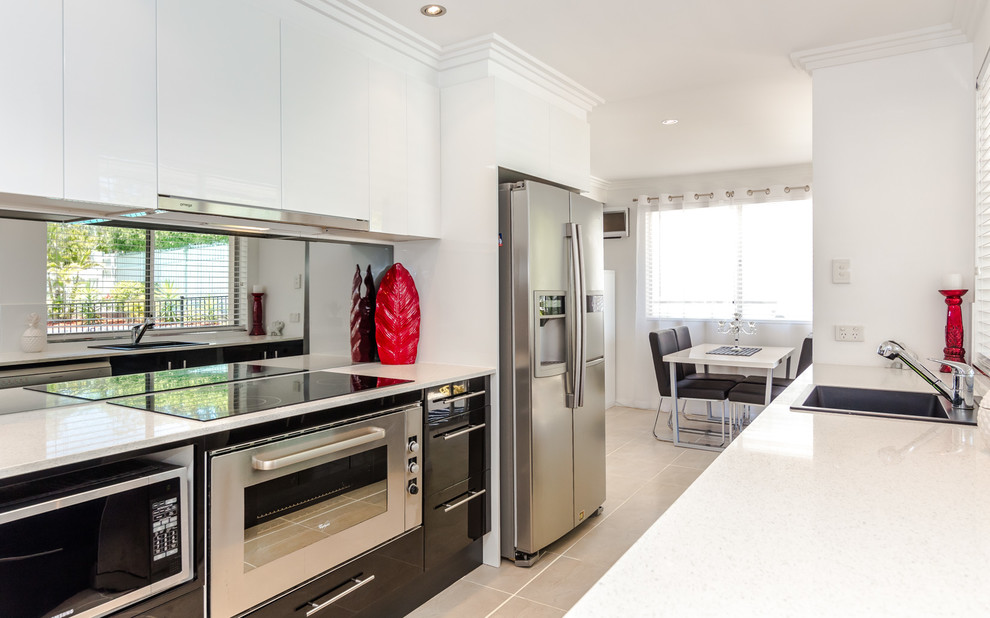 Foto di una cucina minimalista di medie dimensioni con lavello integrato, ante bianche, top in granito, paraspruzzi a specchio, elettrodomestici bianchi e pavimento in terracotta