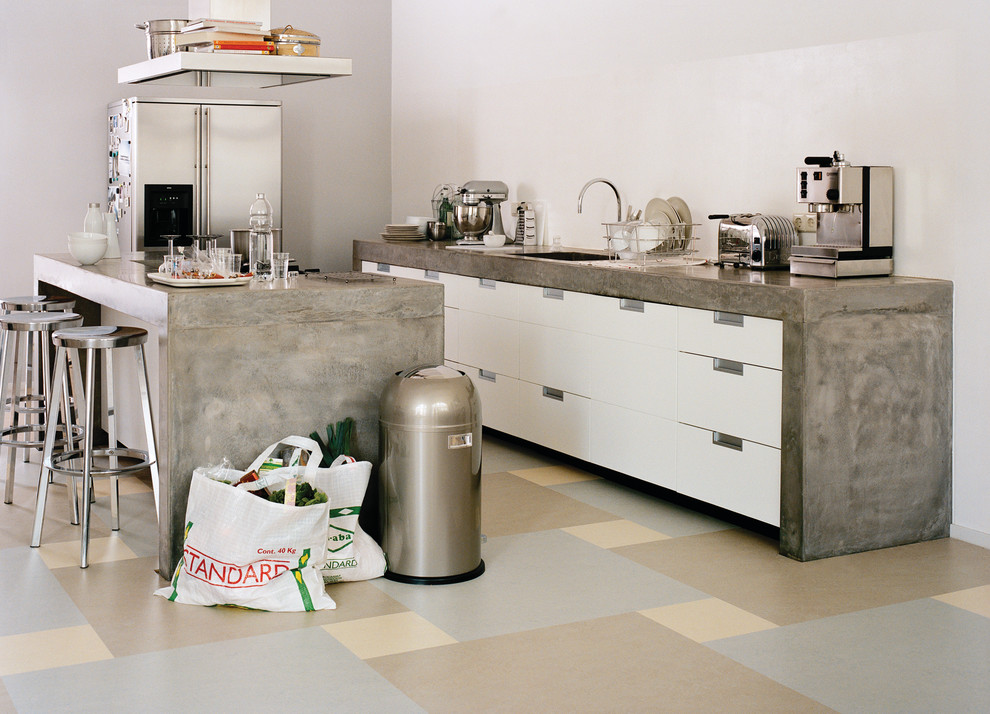 Cette image montre une cuisine américaine parallèle minimaliste de taille moyenne avec un sol en linoléum, des portes de placard blanches, une crédence blanche, un électroménager en acier inoxydable et îlot.