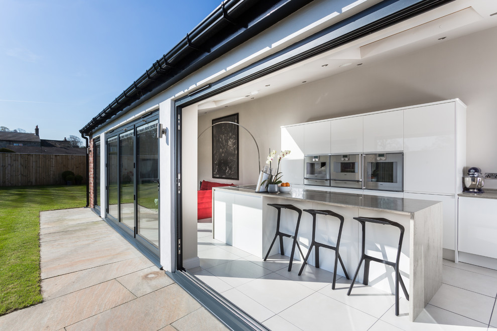 Inspiration for a contemporary galley open plan kitchen in Other with an island, flat-panel cabinets, white cabinets, stainless steel appliances and concrete worktops.