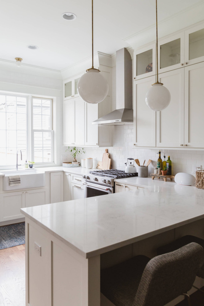 Design ideas for a traditional u-shaped kitchen in San Francisco with a belfast sink, shaker cabinets, white cabinets, white splashback, stainless steel appliances, medium hardwood flooring, a breakfast bar, brown floors and white worktops.
