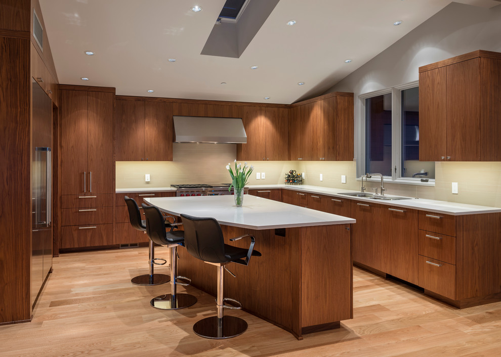 Foto di una cucina a L design con lavello a tripla vasca, ante lisce, ante in legno bruno e elettrodomestici in acciaio inossidabile