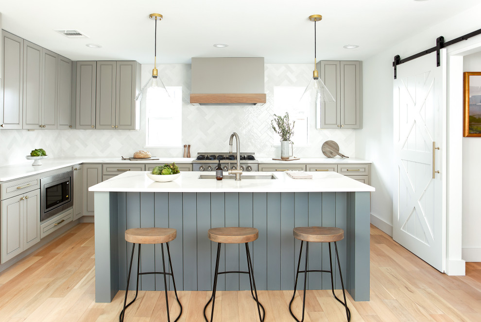 Inspiration for a traditional l-shaped kitchen in Dallas with a submerged sink, raised-panel cabinets, grey cabinets, white splashback, stainless steel appliances, medium hardwood flooring, an island, brown floors and white worktops.