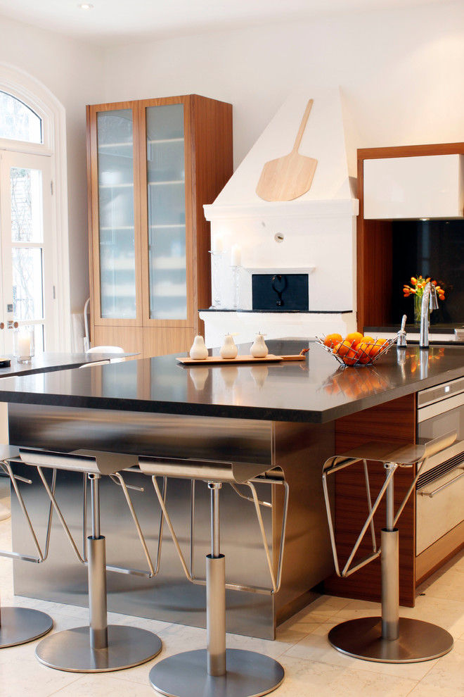 Стильный дизайн: угловая кухня в современном стиле с техникой из нержавеющей стали, обеденным столом, врезной мойкой, плоскими фасадами, светлыми деревянными фасадами, столешницей из кварцевого агломерата и черным фартуком - последний тренд