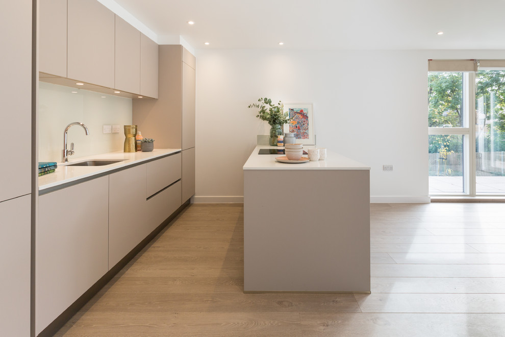 This is an example of a medium sized modern galley open plan kitchen in Gloucestershire with a submerged sink, flat-panel cabinets, brown cabinets, quartz worktops, glass sheet splashback, integrated appliances, laminate floors, no island, brown floors and white worktops.