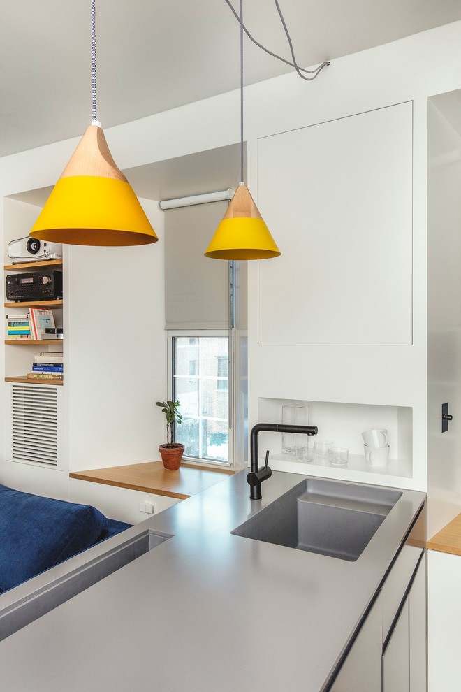 Immagine di una piccola cucina minimalista con lavello integrato, ante lisce, ante grigie, top in superficie solida, parquet chiaro e penisola