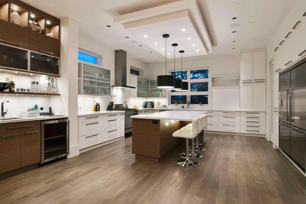 Moderne Wohnküche in U-Form mit Unterbauwaschbecken, flächenbündigen Schrankfronten, weißen Schränken, Küchenrückwand in Weiß, Küchengeräten aus Edelstahl, braunem Holzboden, Quarzit-Arbeitsplatte und Rückwand aus Keramikfliesen in Vancouver