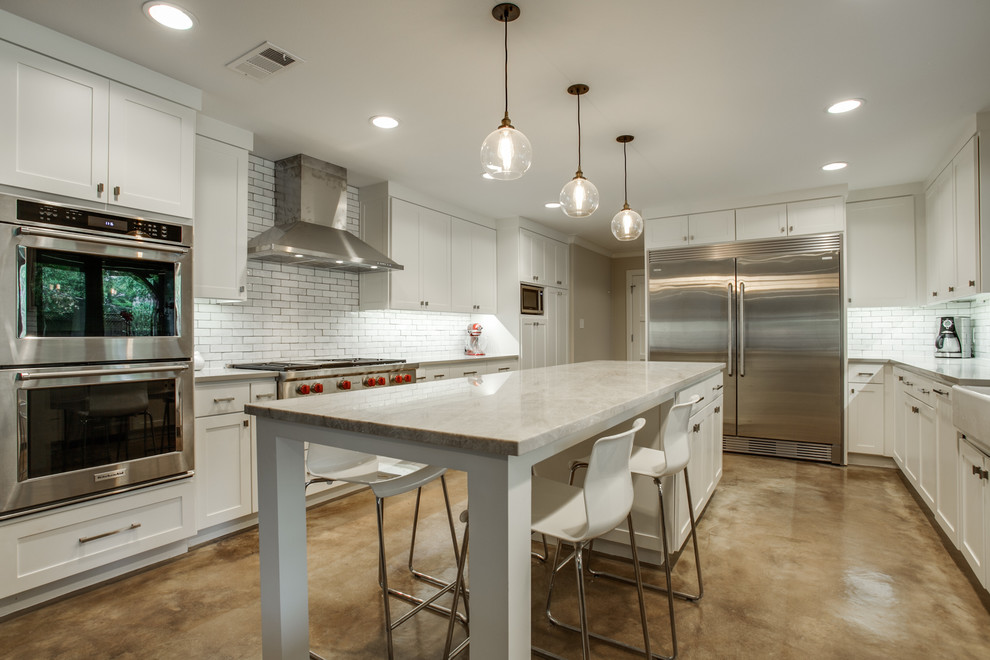 Inspiration for a large contemporary u-shaped concrete floor and brown floor eat-in kitchen remodel in Dallas with a farmhouse sink, shaker cabinets, white cabinets, solid surface countertops, white backsplash, subway tile backsplash, stainless steel appliances and an island
