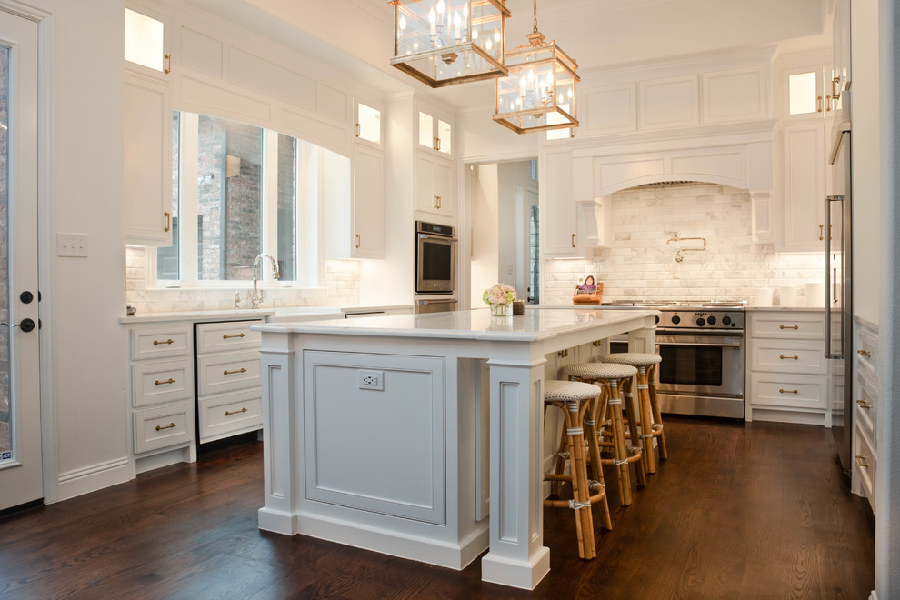 Klassisk inredning av ett mycket stort vit vitt u-kök, med en rustik diskho, skåp i shakerstil, vita skåp, bänkskiva i kvarts, vitt stänkskydd, stänkskydd i marmor, rostfria vitvaror, mörkt trägolv, en köksö och brunt golv