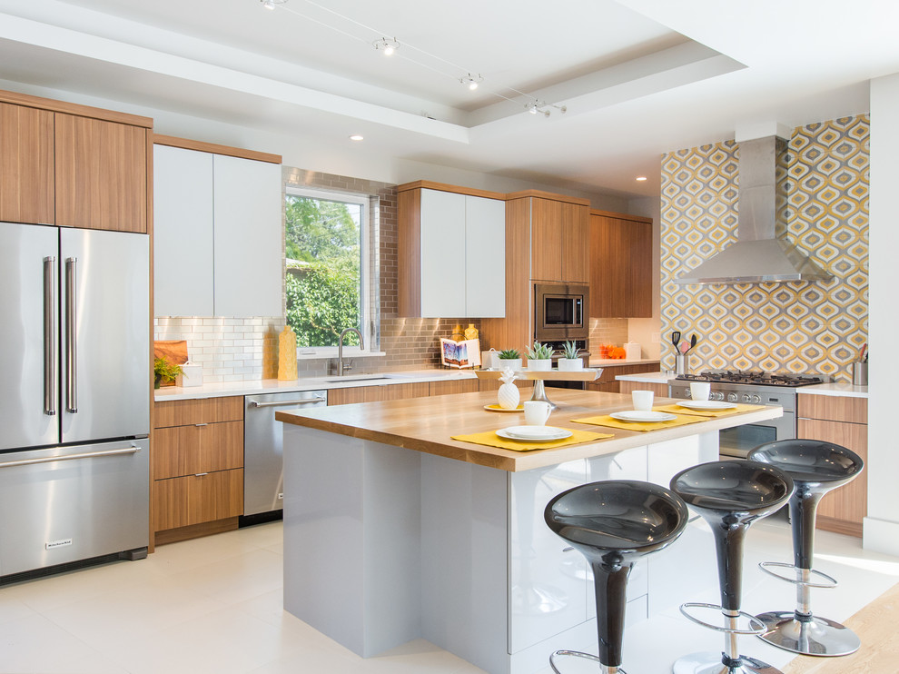 Bild på ett funkis vit vitt l-kök, med en undermonterad diskho, släta luckor, skåp i ljust trä, träbänkskiva, gult stänkskydd, rostfria vitvaror, en köksö och vitt golv