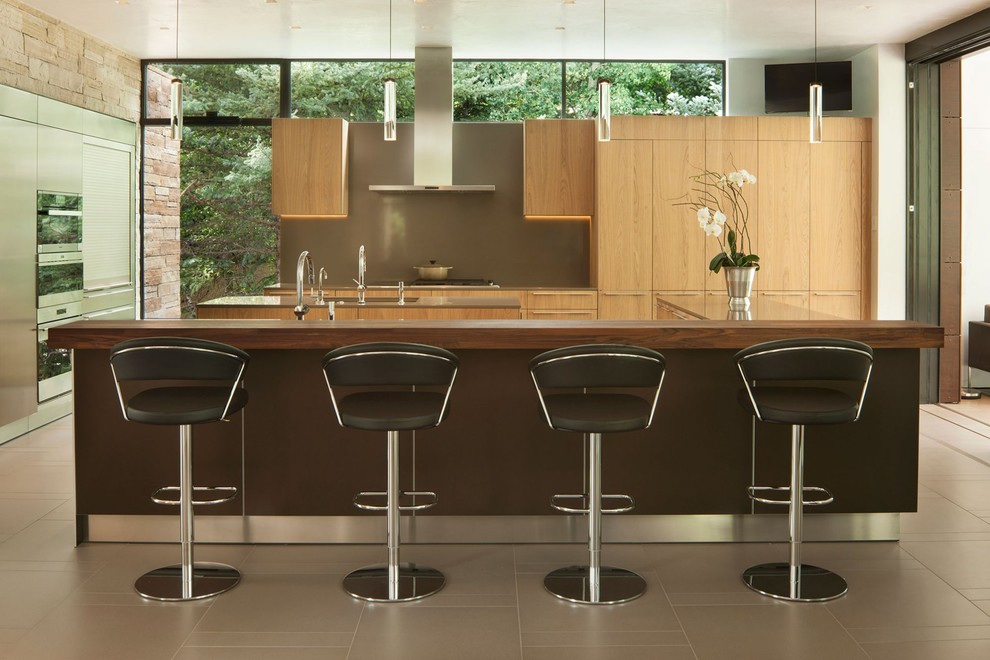 Cette image montre une cuisine minimaliste en bois clair avec un placard à porte plane, une crédence marron, un électroménager en acier inoxydable, un sol marron, un plan de travail marron et 2 îlots.