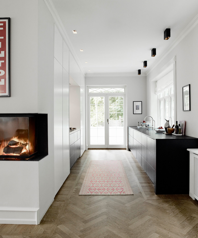 Mittelgroße Moderne Küche ohne Insel mit flächenbündigen Schrankfronten, schwarzen Schränken und braunem Holzboden in London