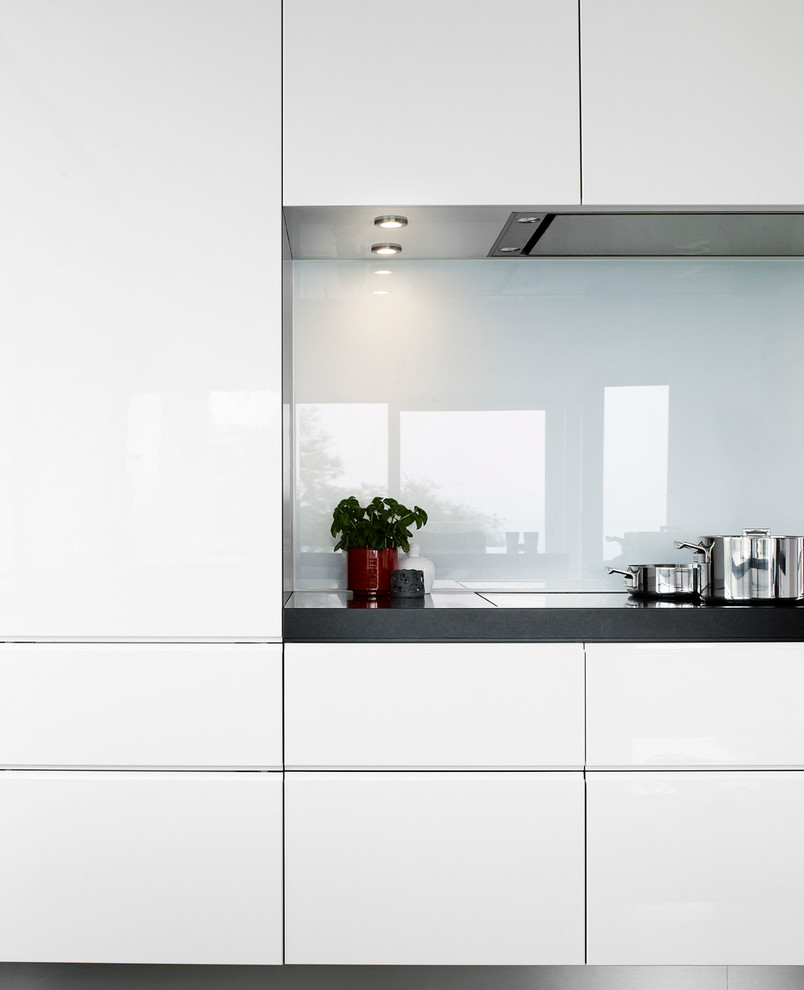 Immagine di un'ampia cucina ad ambiente unico minimal con ante lisce, ante bianche, top in granito, paraspruzzi bianco, paraspruzzi con lastra di vetro, elettrodomestici neri, pavimento con piastrelle in ceramica e penisola