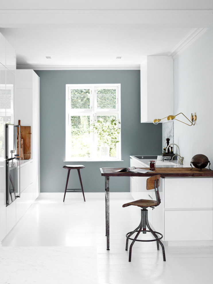 Cette image montre une cuisine design de taille moyenne avec un évier intégré, un placard à porte plane, des portes de placard blanches, un plan de travail en bois et un sol blanc.