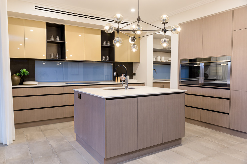 Идея дизайна: кухня-гостиная в современном стиле с накладной мойкой, синим фартуком, фартуком из стекла, черной техникой, полом из керамической плитки, островом и серым полом