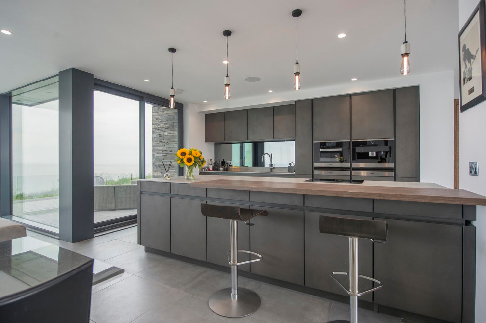 Modern inredning av ett grå linjärt grått kök med öppen planlösning, med en köksö, en undermonterad diskho, släta luckor, grå skåp, svarta vitvaror och grått golv