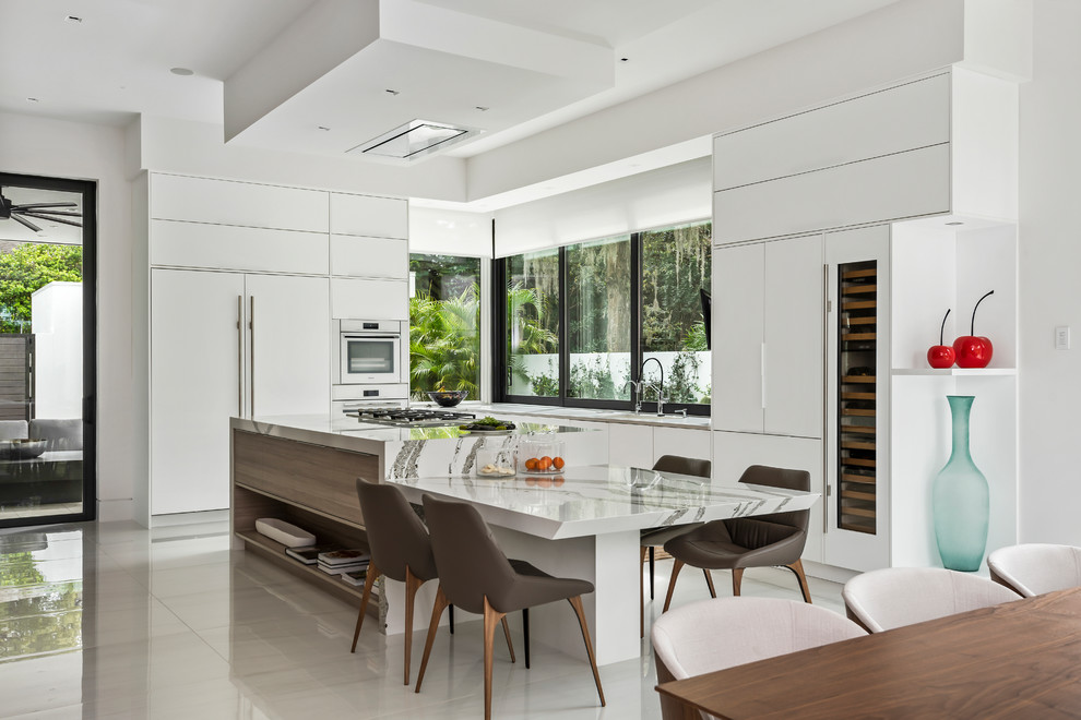 Inredning av ett modernt vit vitt kök och matrum, med släta luckor, vita skåp, fönster som stänkskydd, integrerade vitvaror, en köksö och vitt golv