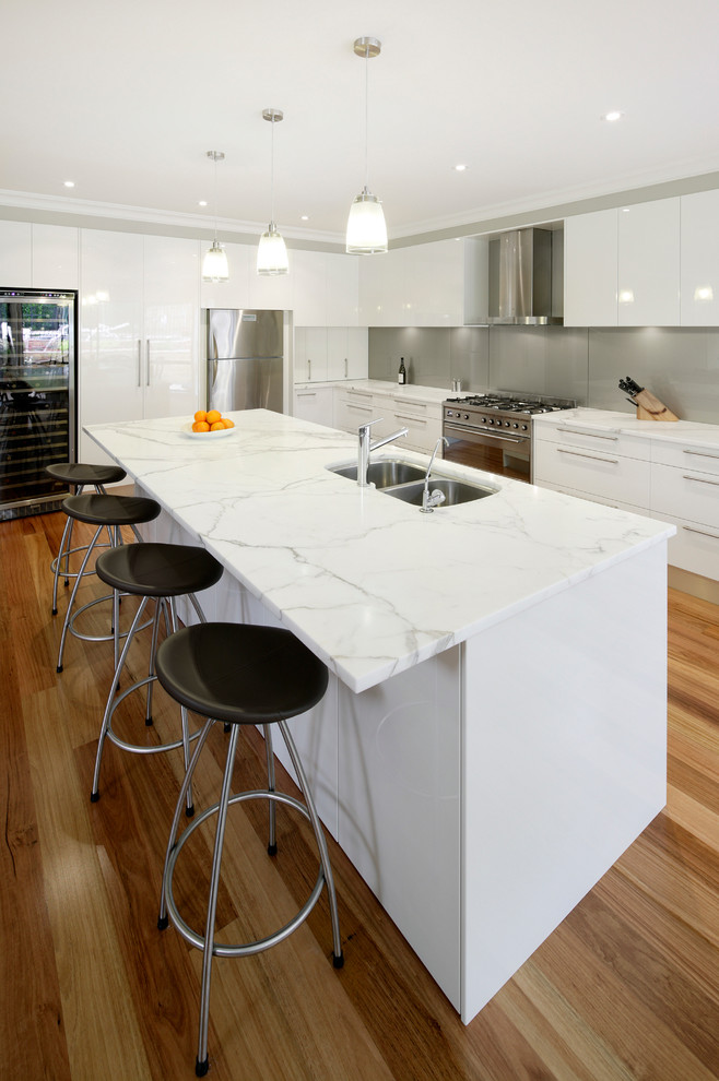 Immagine di una cucina moderna di medie dimensioni con lavello sottopiano, ante bianche, top in marmo, paraspruzzi a effetto metallico, paraspruzzi con lastra di vetro, elettrodomestici in acciaio inossidabile e parquet chiaro