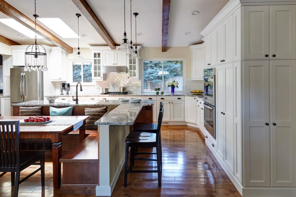 Example of a large transitional l-shaped medium tone wood floor eat-in kitchen design in San Diego with an undermount sink, recessed-panel cabinets, white cabinets, quartz countertops, white backsplash, glass tile backsplash, stainless steel appliances and an island