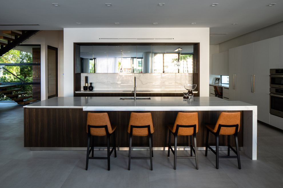 Eat-in kitchen - huge contemporary l-shaped concrete floor and white floor eat-in kitchen idea in Miami with a drop-in sink, flat-panel cabinets, white cabinets, marble countertops, white backsplash, marble backsplash, paneled appliances, an island and white countertops