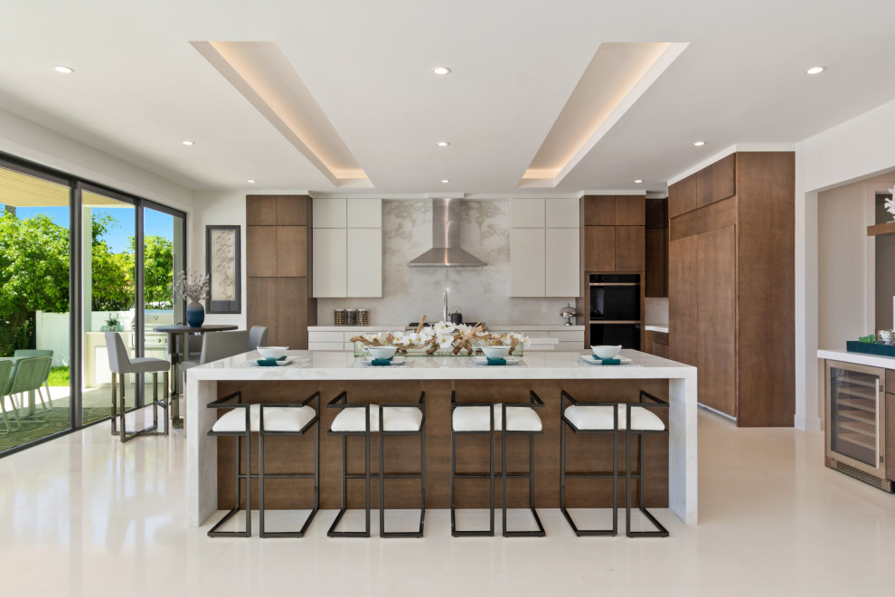 マイアミにあるコンテンポラリースタイルのおしゃれなキッチン (フラットパネル扉のキャビネット、中間色木目調キャビネット、白いキッチンパネル、シルバーの調理設備、白い床、白いキッチンカウンター) の写真