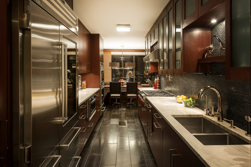 Inspiration for a timeless galley eat-in kitchen remodel in New York with a double-bowl sink, glass-front cabinets, dark wood cabinets, black backsplash and stainless steel appliances