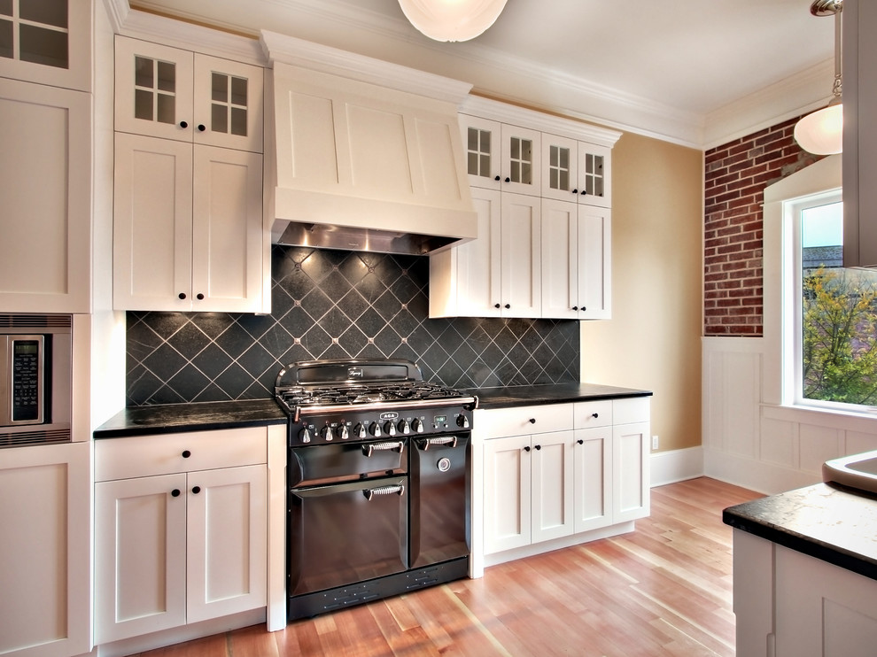 Foto på ett lantligt kök, med skåp i shakerstil, vita skåp, svart stänkskydd, stänkskydd i stenkakel och svarta vitvaror