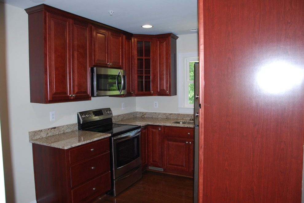 This is an example of a medium sized classic u-shaped enclosed kitchen in DC Metro with a submerged sink, raised-panel cabinets, dark wood cabinets, granite worktops, stainless steel appliances, dark hardwood flooring, no island, brown floors and beige worktops.