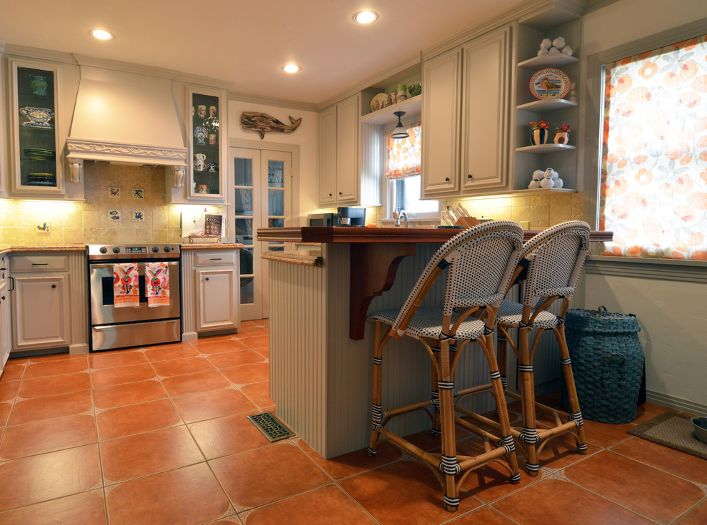 Immagine di una cucina a L eclettica con ante con bugna sagomata, ante grigie, paraspruzzi beige, elettrodomestici in acciaio inossidabile, pavimento in terracotta e penisola
