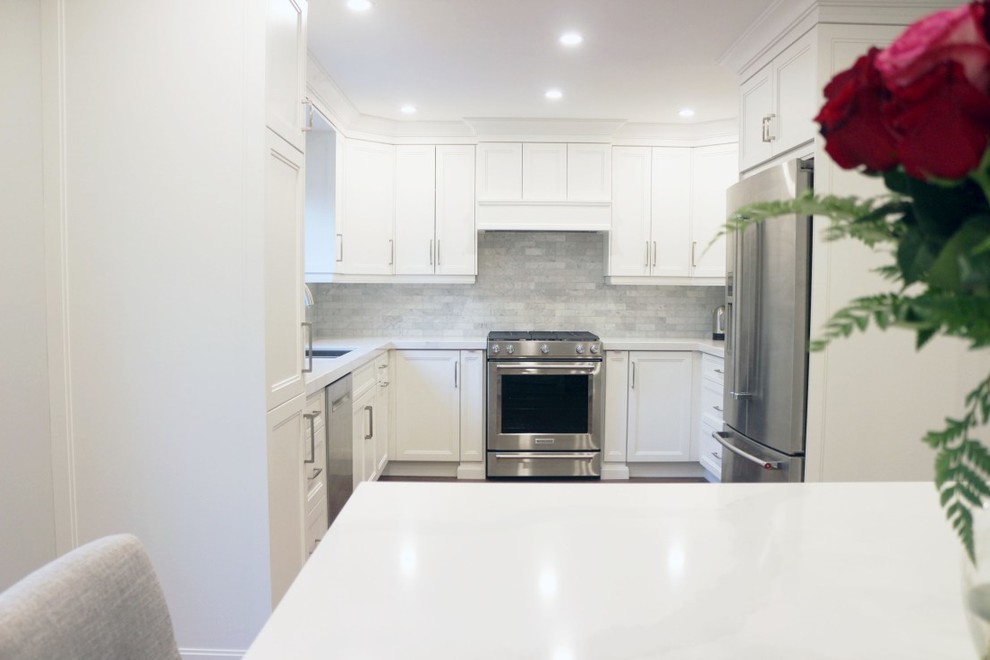 Inredning av ett klassiskt mellanstort vit vitt kök, med en undermonterad diskho, skåp i shakerstil, vita skåp, bänkskiva i kvartsit, vitt stänkskydd, stänkskydd i keramik, rostfria vitvaror, mellanmörkt trägolv, en köksö och brunt golv