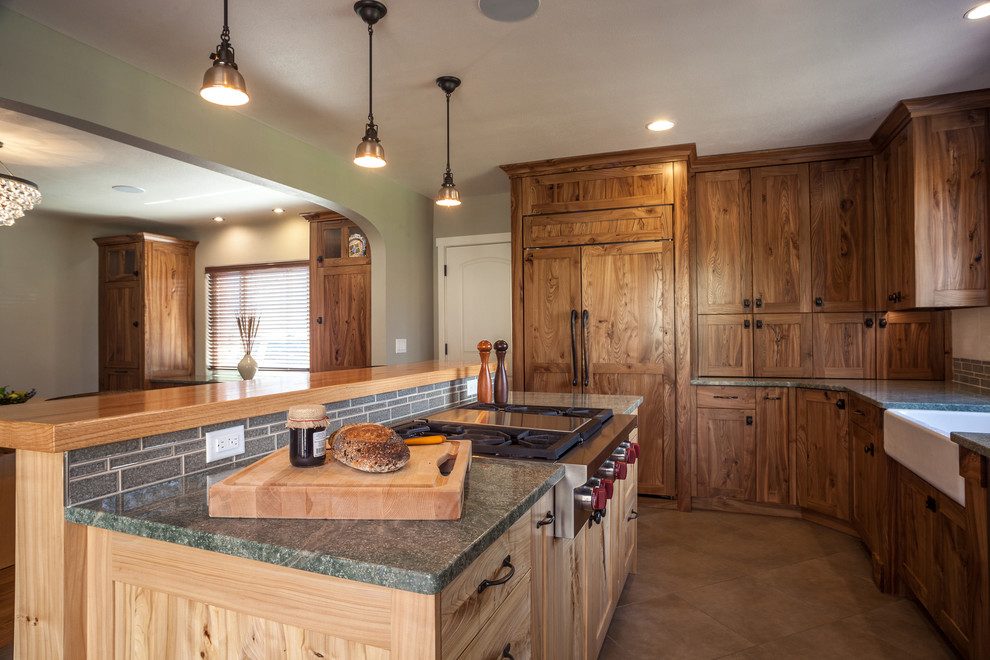 Example of a mid-sized arts and crafts l-shaped porcelain tile eat-in kitchen design in Other with a farmhouse sink, medium tone wood cabinets, granite countertops, green backsplash, glass tile backsplash, paneled appliances and an island