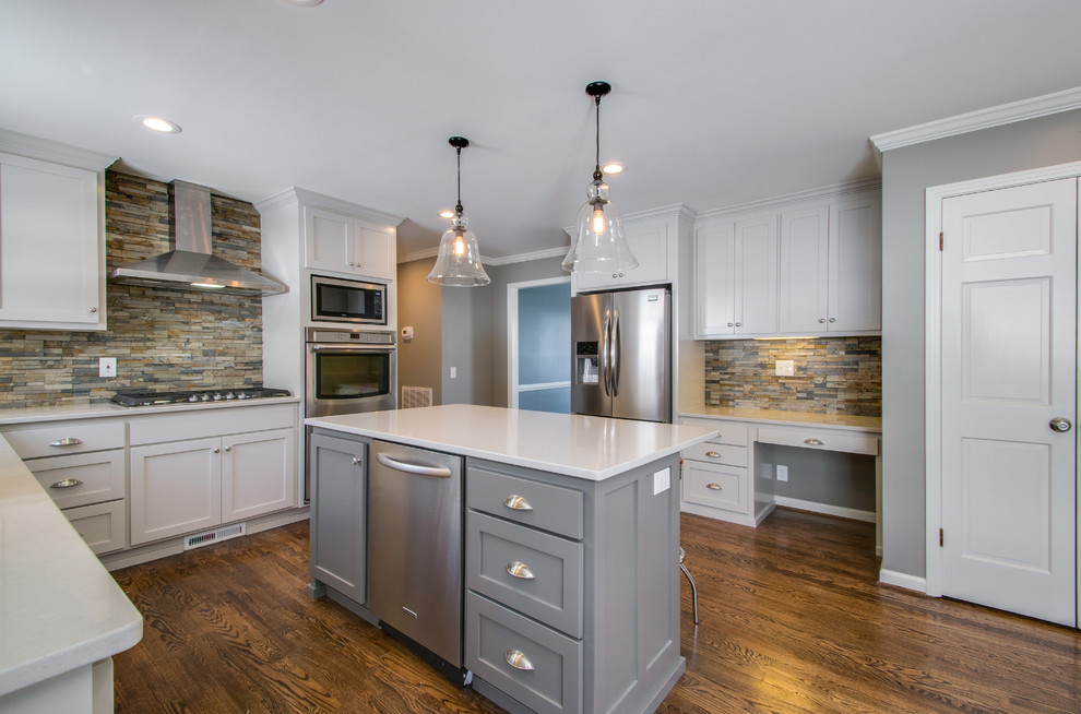 This is an example of a medium sized traditional l-shaped enclosed kitchen in Nashville with a submerged sink, recessed-panel cabinets, grey cabinets, engineered stone countertops, brown splashback, stone tiled splashback, stainless steel appliances, dark hardwood flooring and an island.