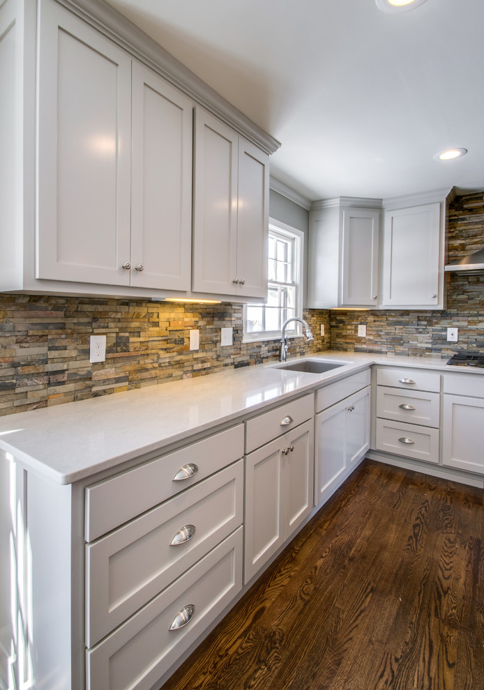 Photo of a medium sized classic l-shaped enclosed kitchen in Nashville with a submerged sink, recessed-panel cabinets, grey cabinets, engineered stone countertops, brown splashback, stone tiled splashback, stainless steel appliances, dark hardwood flooring and an island.
