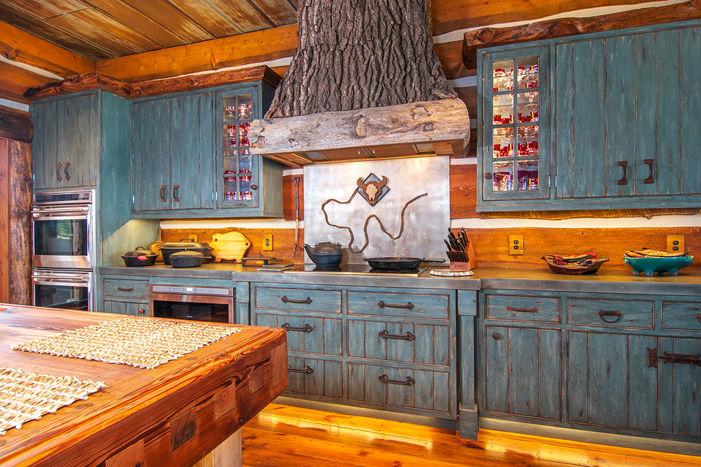 Exemple d'une grande cuisine encastrable montagne en U et bois vieilli fermée avec un placard à porte persienne, un plan de travail en zinc, une crédence marron, une crédence en bois, un sol en bois brun et îlot.