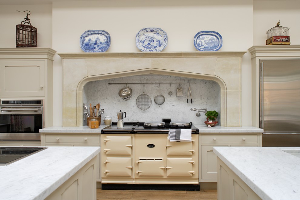 Large traditional galley kitchen/diner in Dorset with an integrated sink, recessed-panel cabinets, white cabinets, marble worktops, white splashback, stone tiled splashback, integrated appliances, light hardwood flooring and multiple islands.