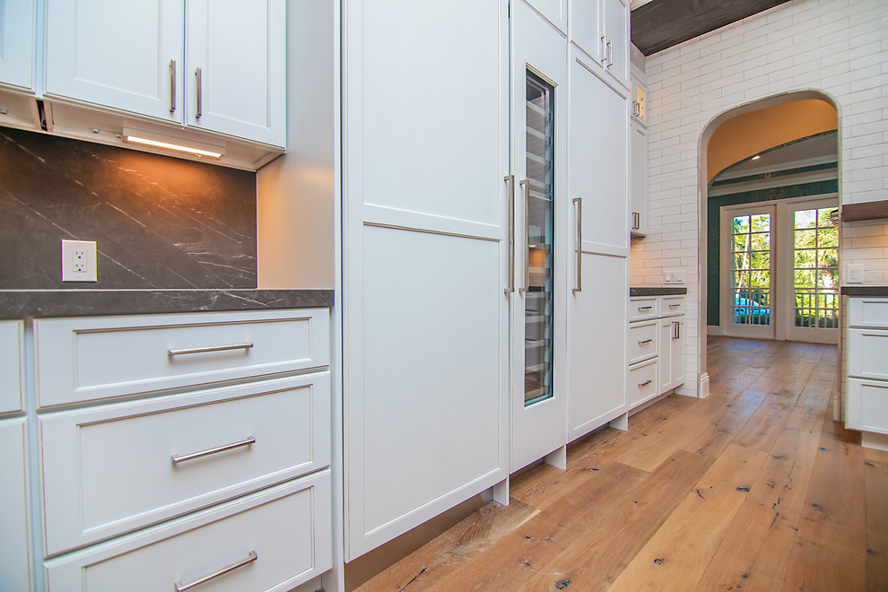 Large cottage l-shaped light wood floor and brown floor eat-in kitchen photo in Miami with an undermount sink, flat-panel cabinets, white backsplash, porcelain backsplash, paneled appliances and an island