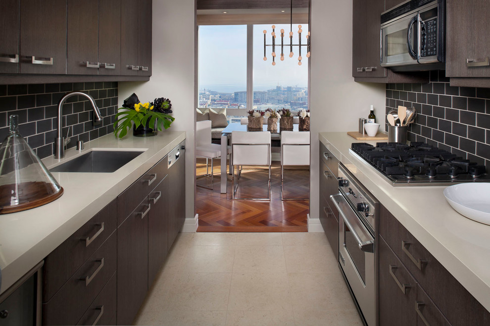 This is an example of a contemporary galley enclosed kitchen in San Francisco with metro tiled splashback, stainless steel appliances, a submerged sink, flat-panel cabinets and dark wood cabinets.