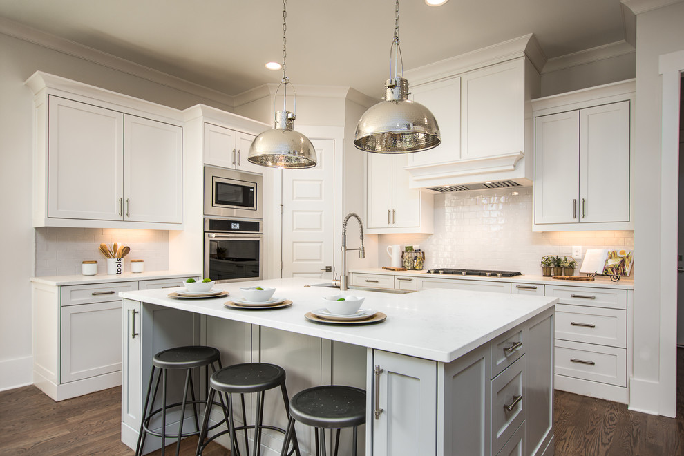 Traditional kitchen in Atlanta with shaker cabinets, white cabinets, white splashback, stainless steel appliances, dark hardwood flooring, an island and white worktops.