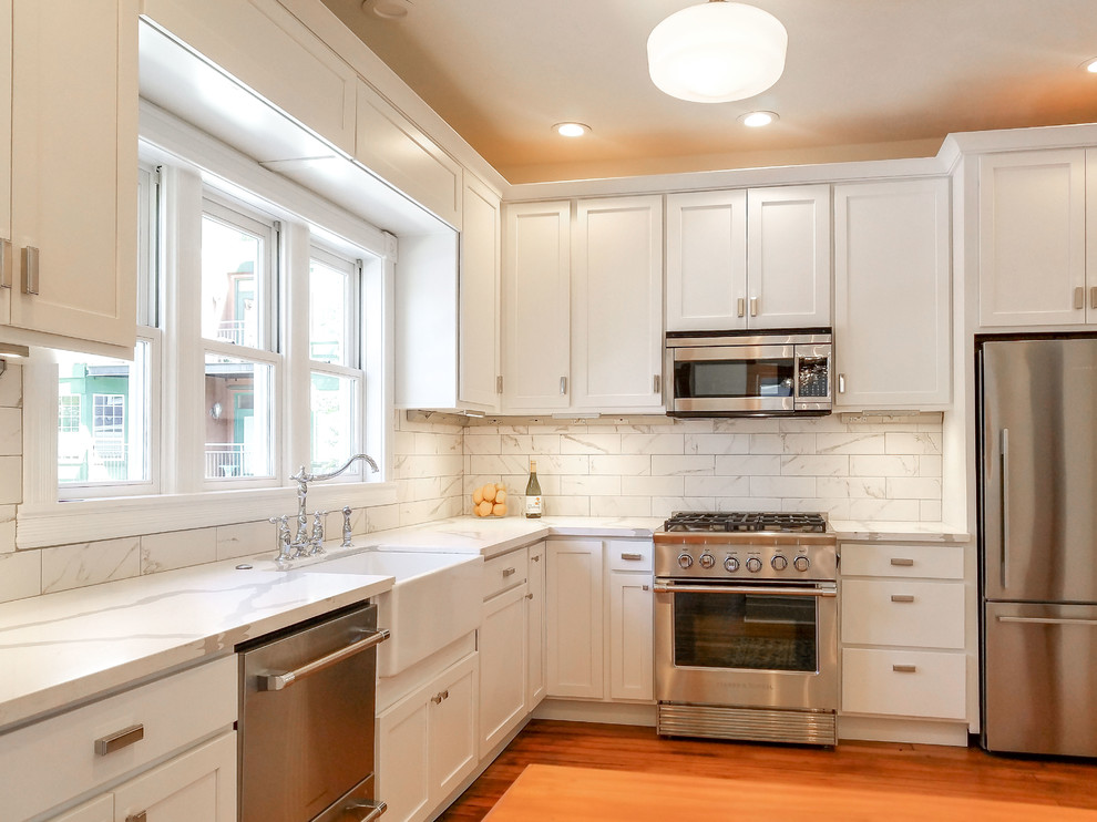 Example of a mid-sized transitional l-shaped medium tone wood floor and brown floor eat-in kitchen design in Boise with a farmhouse sink, shaker cabinets, white cabinets, quartz countertops, white backsplash, ceramic backsplash, stainless steel appliances, no island and white countertops