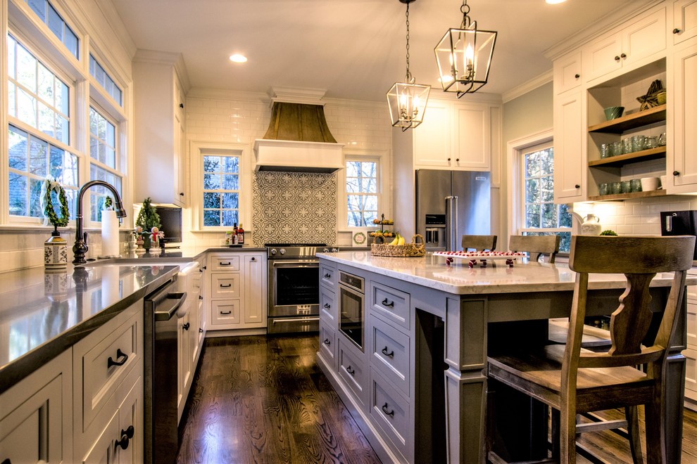 Enclosed kitchen - mid-sized traditional l-shaped dark wood floor and brown floor enclosed kitchen idea in Atlanta with a farmhouse sink, recessed-panel cabinets, white cabinets, quartz countertops, white backsplash, ceramic backsplash, stainless steel appliances, an island and gray countertops