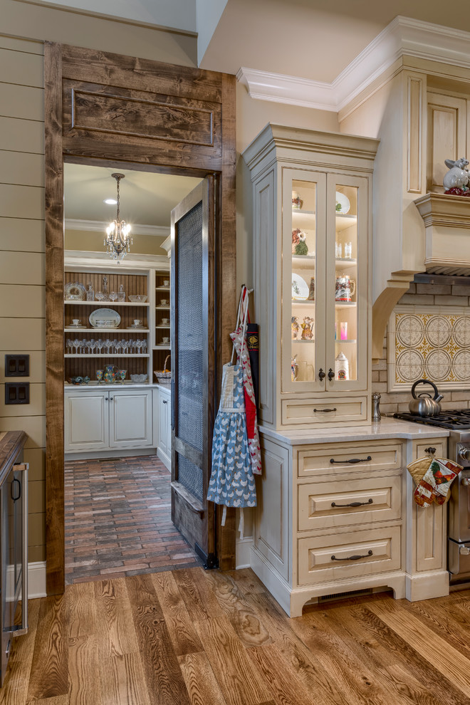 Kitchen pantry - huge farmhouse l-shaped medium tone wood floor and brown floor kitchen pantry idea in Other with a farmhouse sink, raised-panel cabinets, beige cabinets, granite countertops, beige backsplash, ceramic backsplash, paneled appliances, an island and beige countertops