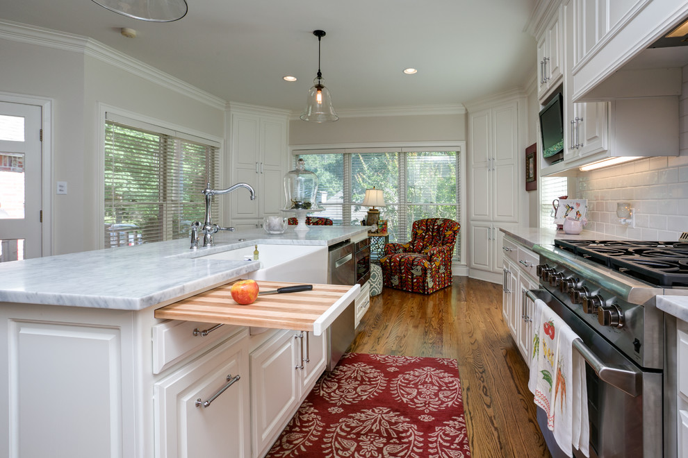 Example of a mid-sized classic l-shaped dark wood floor eat-in kitchen design in Little Rock with a farmhouse sink, raised-panel cabinets, white cabinets, solid surface countertops, white backsplash, stone slab backsplash, stainless steel appliances and an island